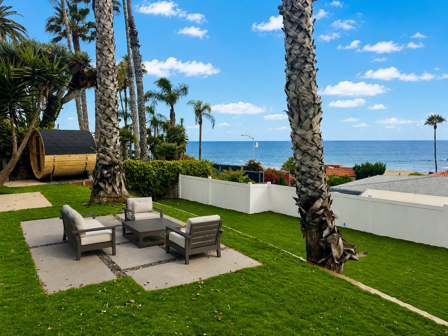 Grassy backyard at Nalu House with lounge seating, palm trees, and an ocean view