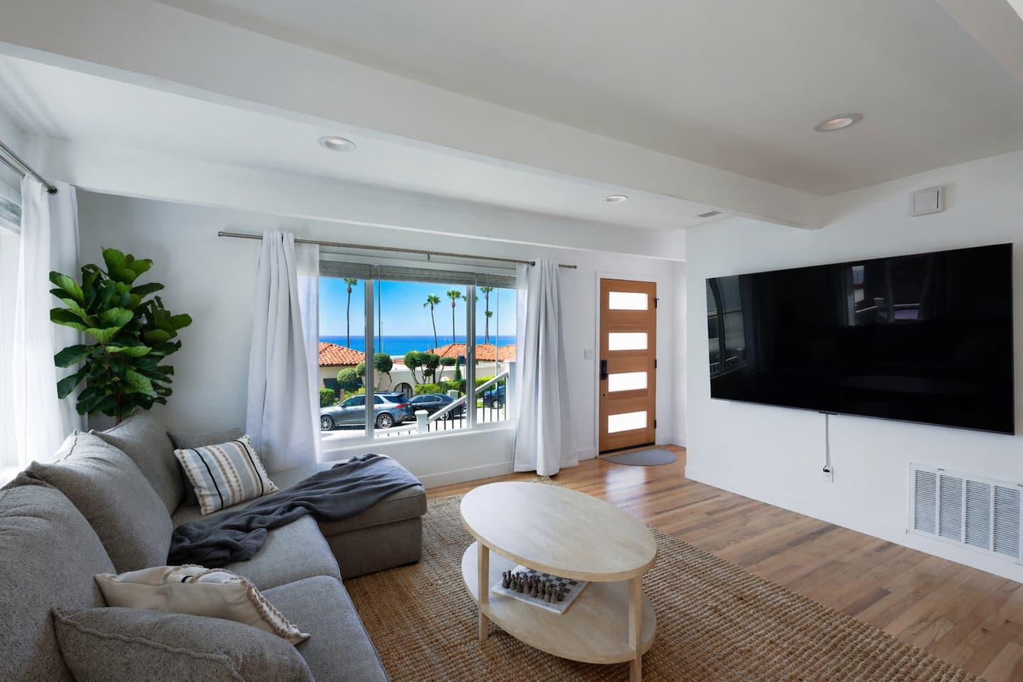 Sunlit living room at Nalu House framing palm trees and the blue Pacific