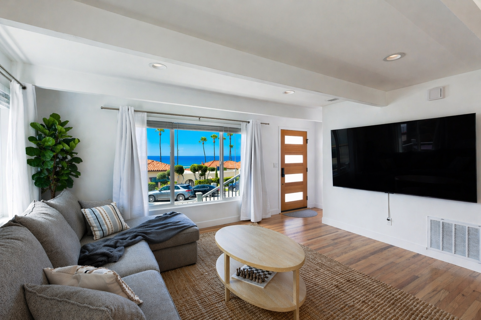 Sunlit living room at Nalu House framing palm trees and the blue Pacific