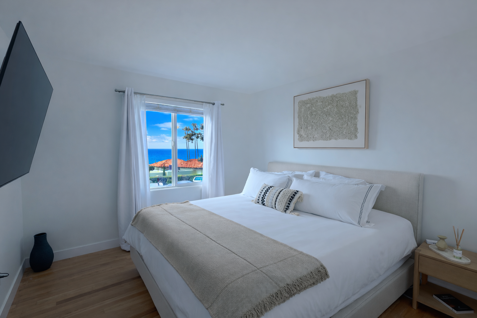 Primary bedroom with a king bed and a window framing palm trees and the ocean
