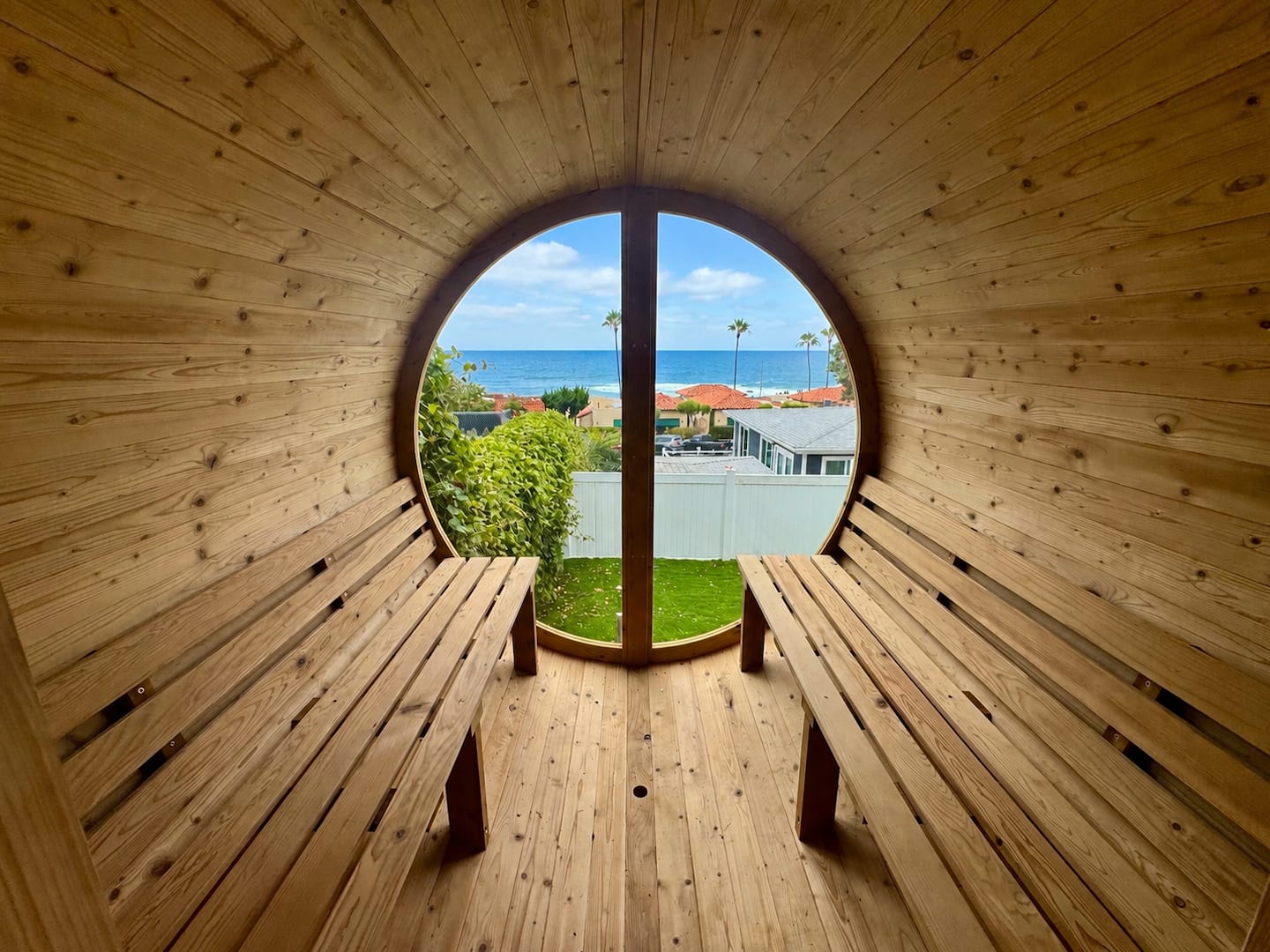 Ocean view framed through the circular window of the backyard barrel sauna at Nalu House